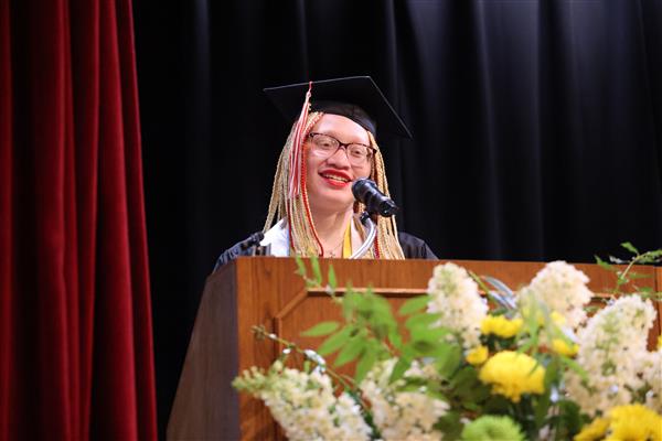 A graduate from the Alabama School for the Blind speaks from behind a podium at graduation. She wears a black cap and gown and a white stole.
